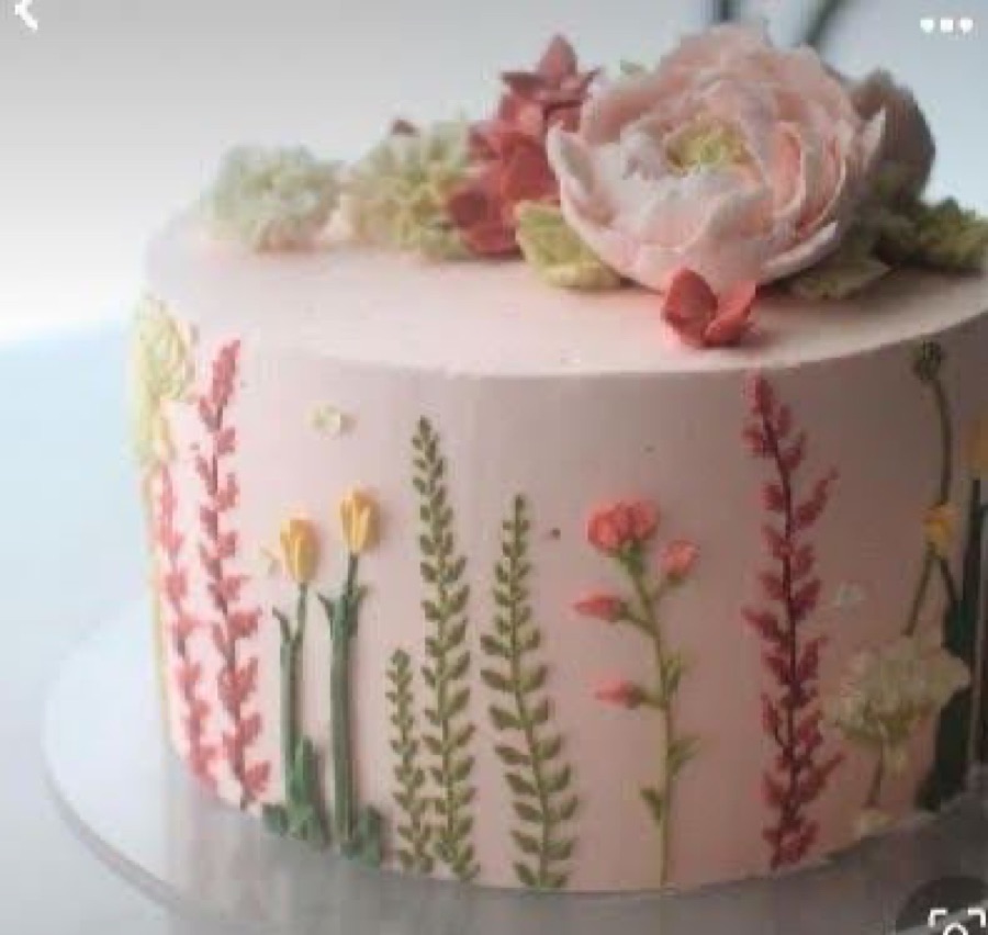A pale pink cake piped with wildflowers and a peony on top